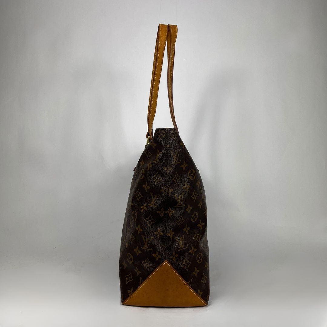 A Louis Vuitton monogram canvas tote bag with tan leather trim and shoulder straps, shown from the side against a neutral gray background.