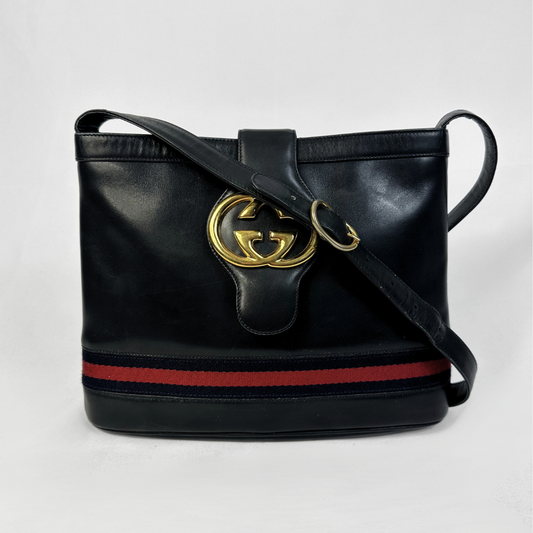 A black leather shoulder bag with a gold-tone interlocking G logo on the front, featuring the signature red and navy blue web stripe along the bottom and a matching web stripe on the strap.