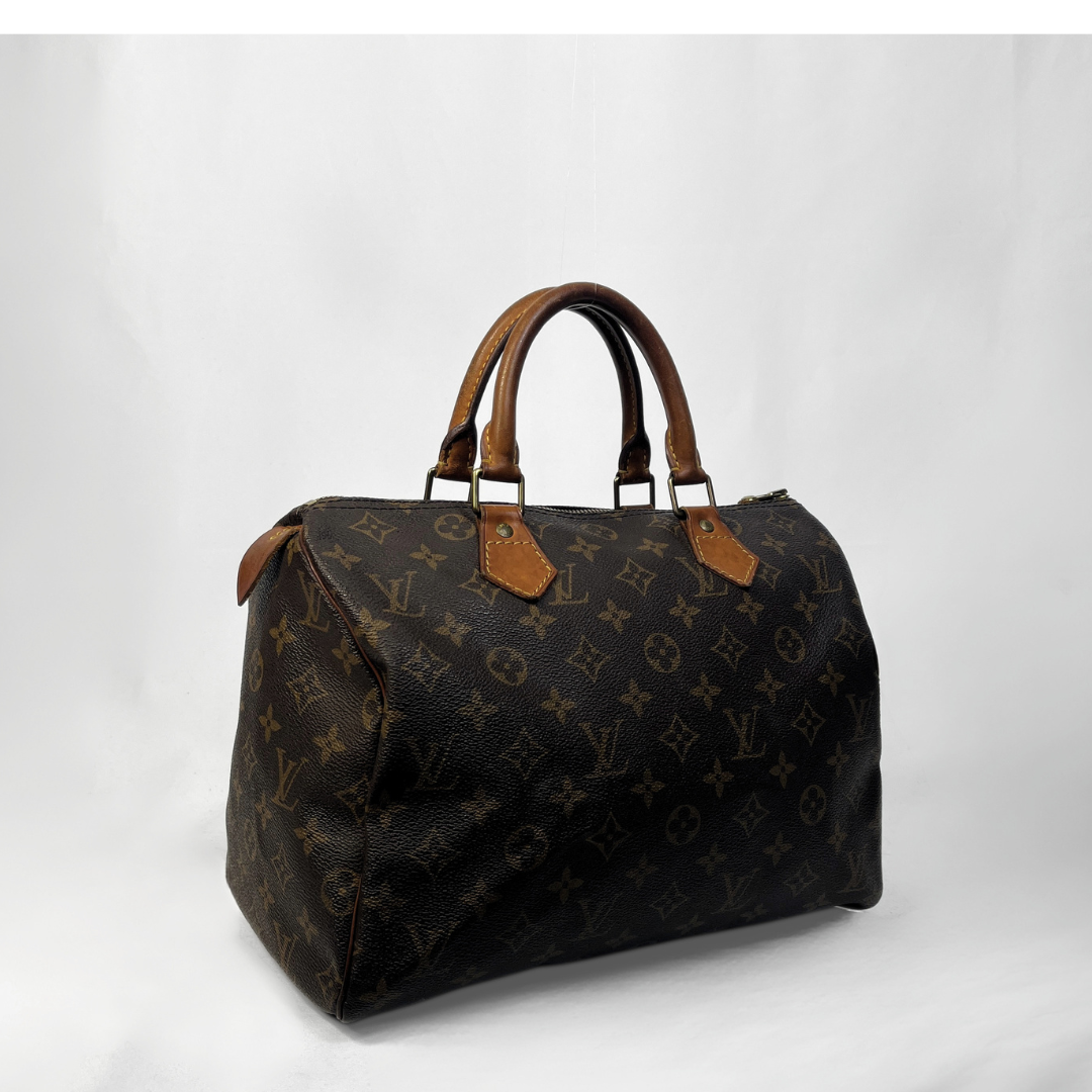 A Louis Vuitton monogram canvas Speedy bag with brown leather handles and trim, photographed against a light gray studio background.