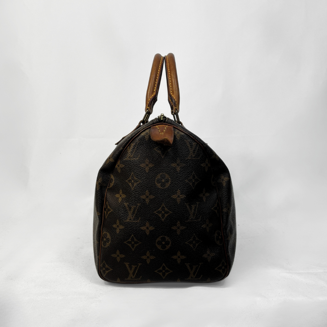A vintage Louis Vuitton monogram Speedy bag in dark brown coated canvas with tan leather handles, photographed against a white fabric backdrop.
