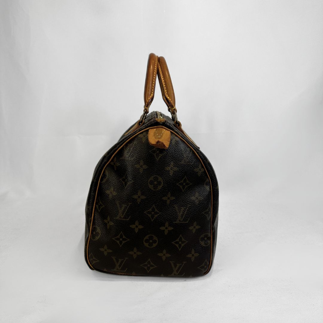 A Louis Vuitton monogram canvas duffle bag in dark brown with tan leather handles and trim, photographed against a white fabric backdrop.