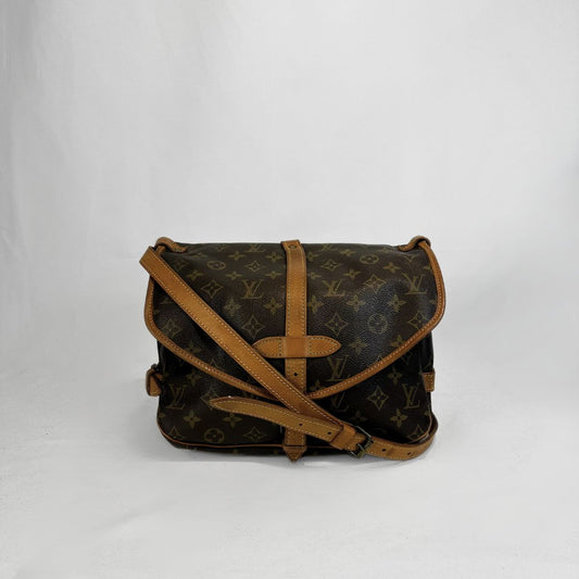 A Louis Vuitton monogram canvas shoulder bag with tan leather trim and strap, photographed against a plain light gray background.