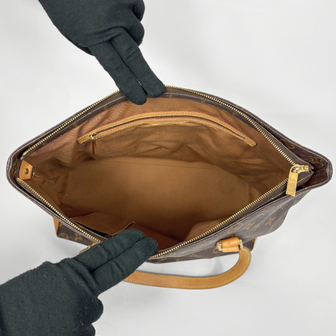 Brown leather handbag with gold zippers held open by a gloved hand on a white background