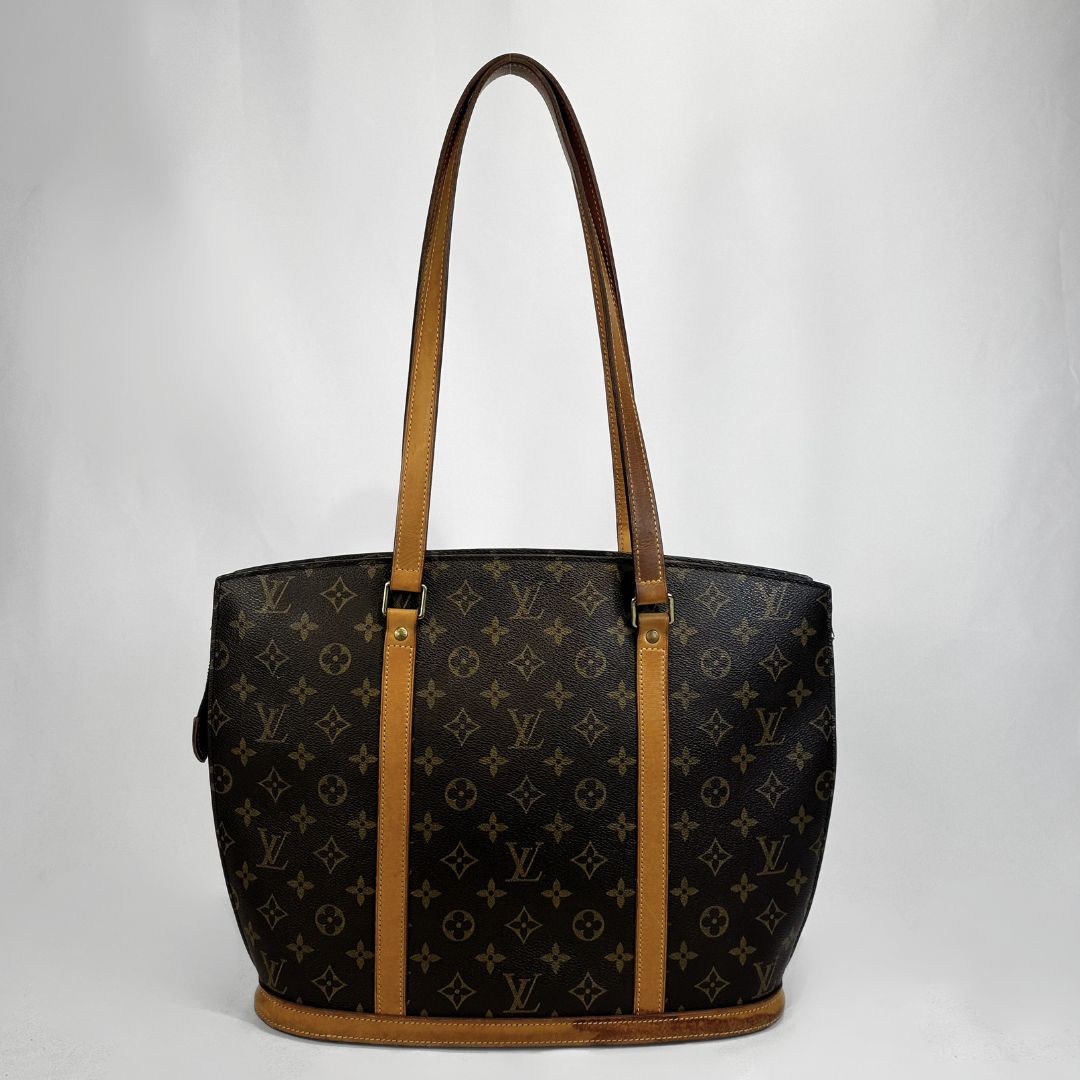 Louis Vuitton monogram canvas tote bag with tan leather shoulder straps and trim, shown against a light gray studio background.