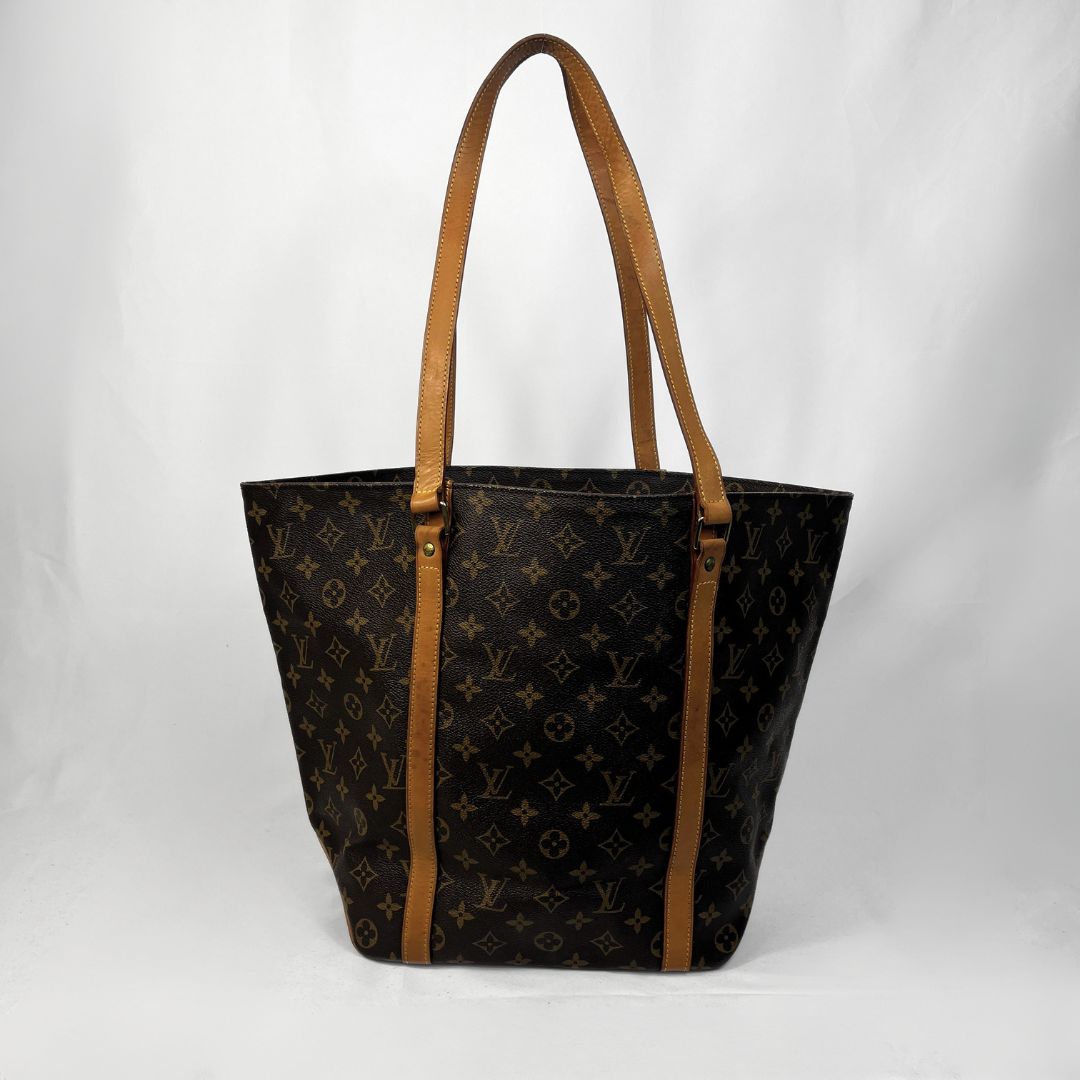 A Louis Vuitton monogram canvas tote bag with tan leather shoulder straps and trim, photographed against a white studio backdrop.