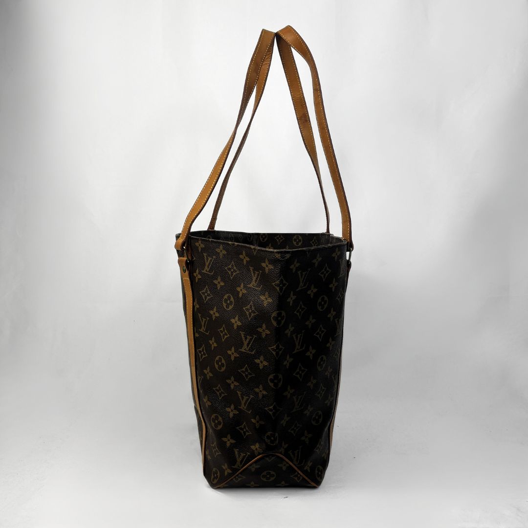 A Louis Vuitton monogram canvas tote bag with brown leather shoulder straps, photographed against a light gray studio background.