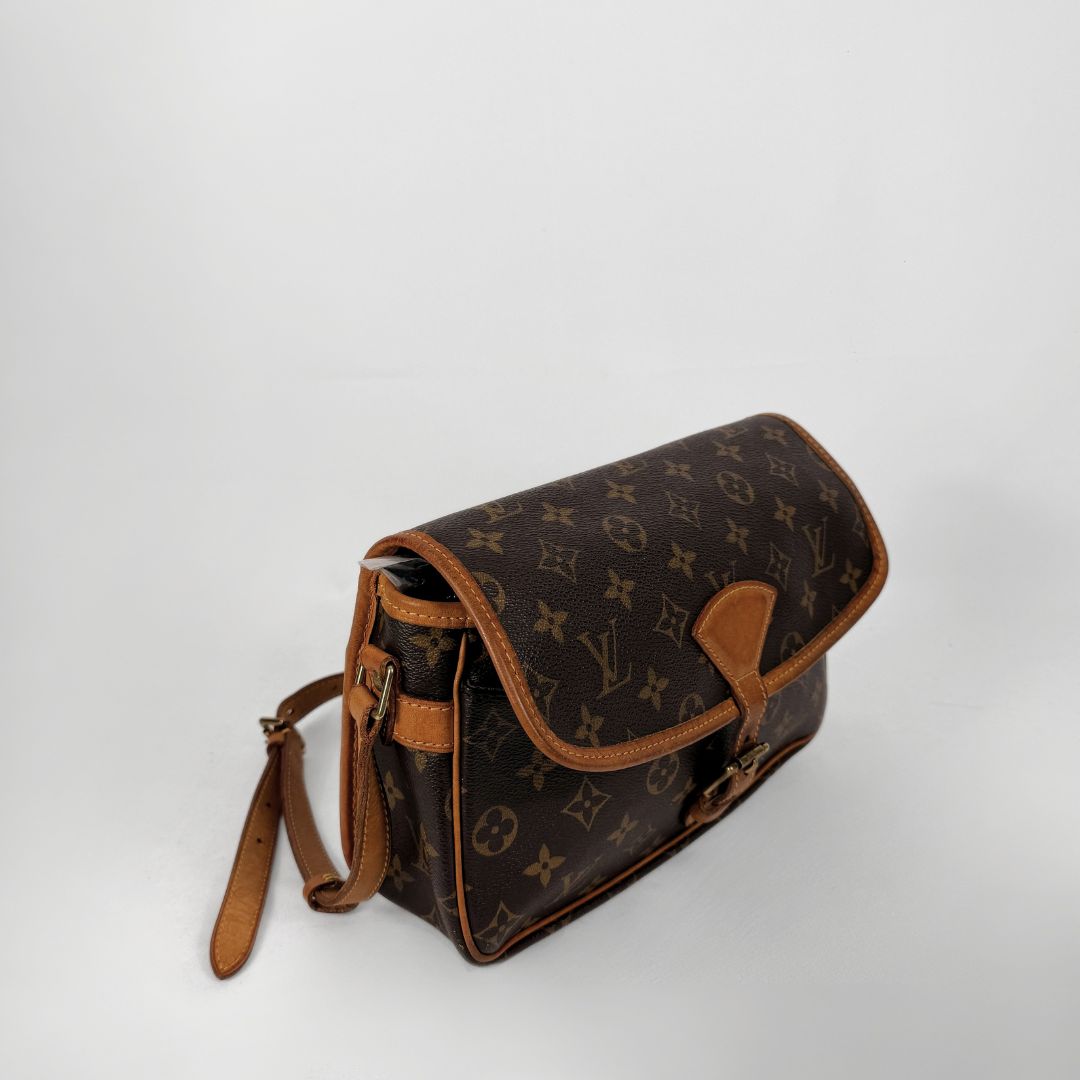 A Louis Vuitton monogram canvas shoulder bag with tan leather trim and strap, photographed on a light gray studio background.