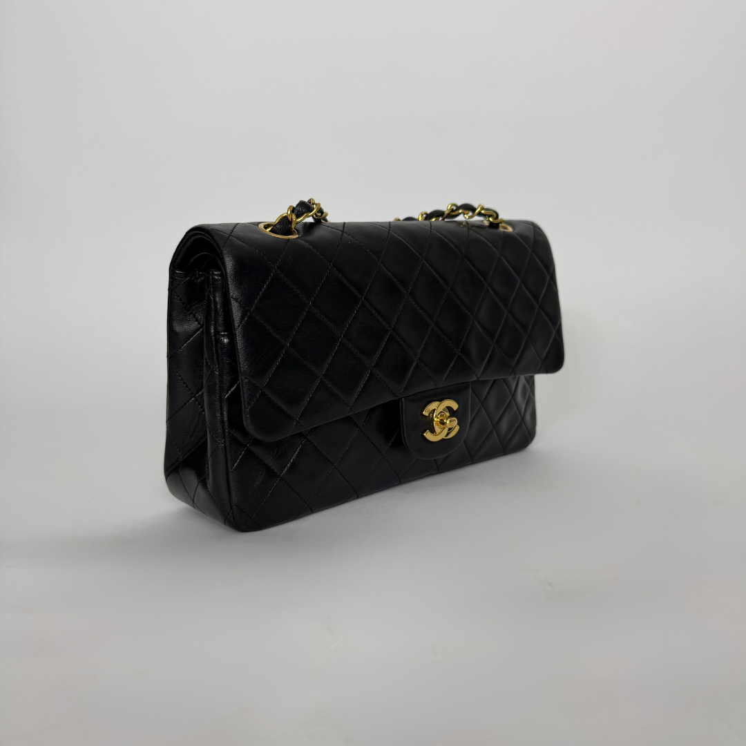 Black quilted handbag with gold chain strap on a light gray background