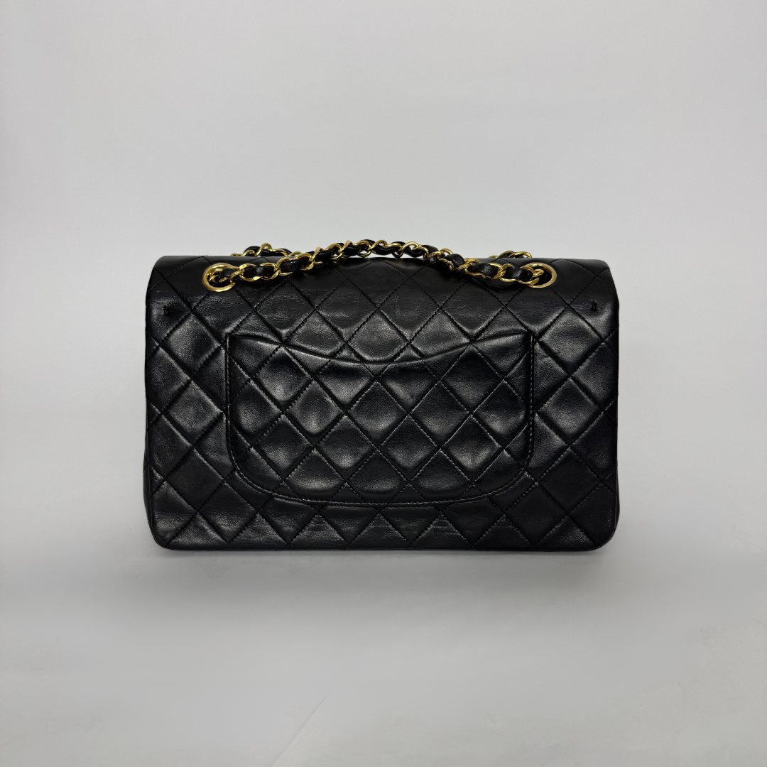 Black quilted handbag with gold chain on a light gray background