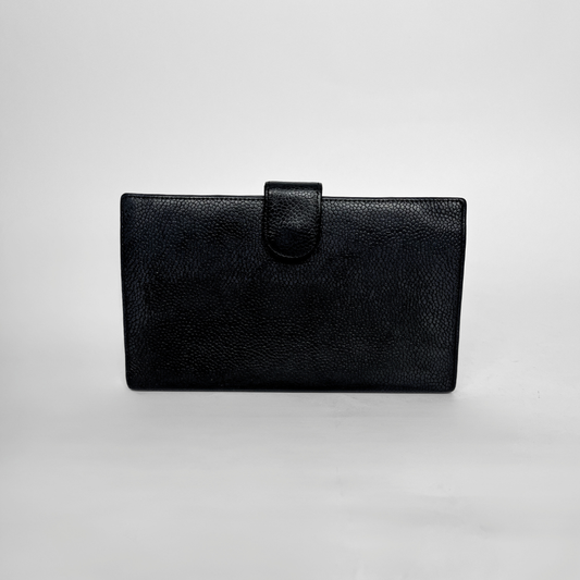 Eine schwarze Clutch-Geldbörse aus strukturiertem Leder mit Riemenverschluss, fotografiert vor einem neutralen hellgrauen Hintergrund.