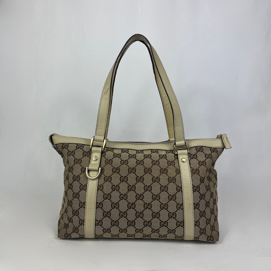 A vintage-style Gucci tote bag featuring the classic brown and beige GG monogram canvas, beige leather trim and handles, and gold-tone hardware, photographed against a neutral light gray background.