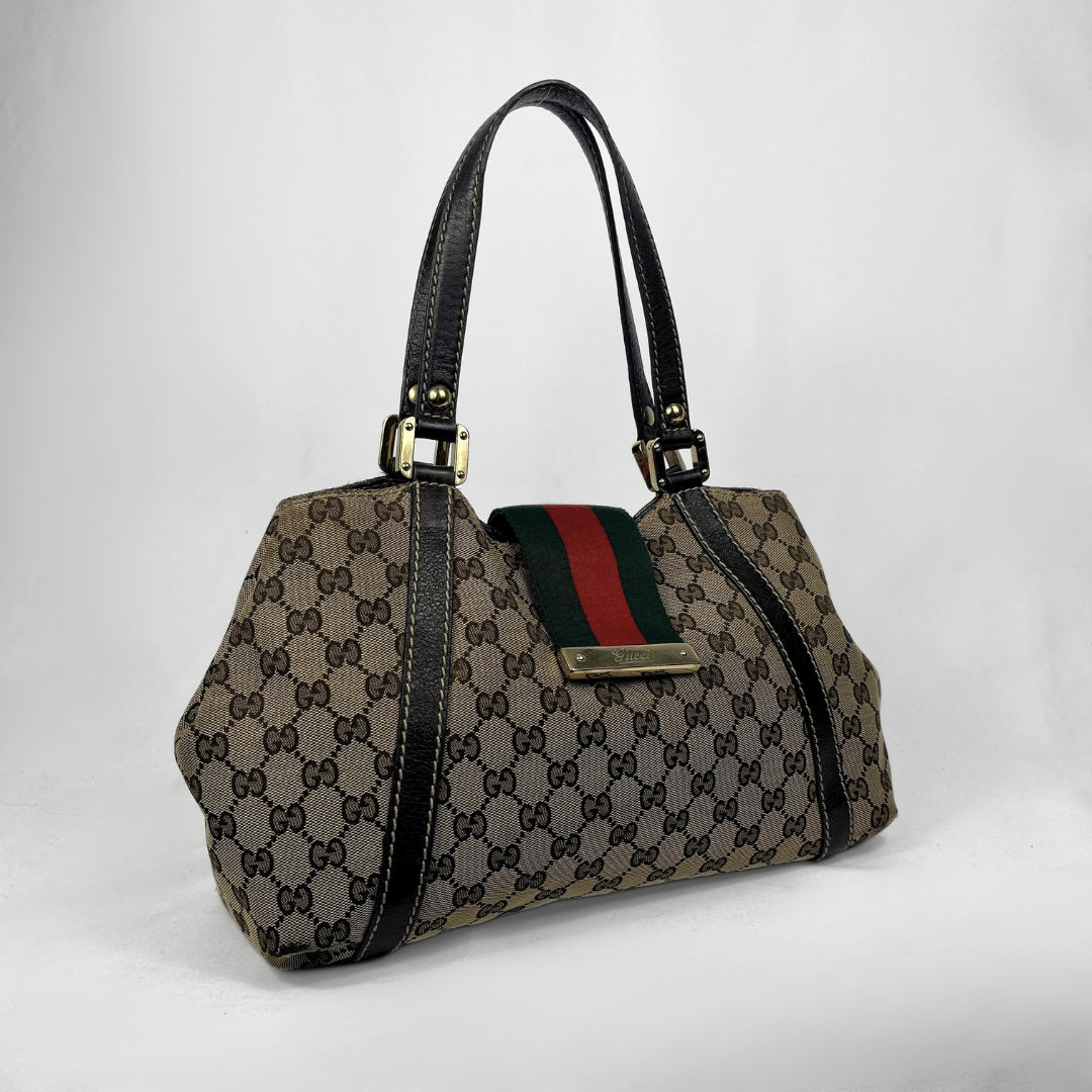 A vintage-style Gucci shoulder bag in brown GG Supreme canvas with black leather trim, gold-tone hardware, and the signature green and red web stripe detail on the front flap.