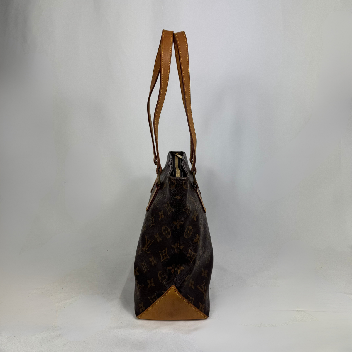 A Louis Vuitton monogram tote bag in dark brown coated canvas with tan leather trim and shoulder straps, shown standing upright against a light gray studio background.