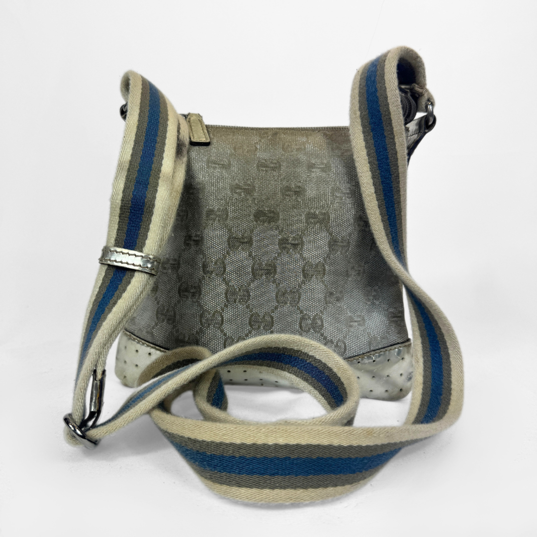 A Gucci GG canvas crossbody bag in metallic silver with a blue and beige striped shoulder strap, silver-tone hardware and a studded base, photographed against a plain white background.