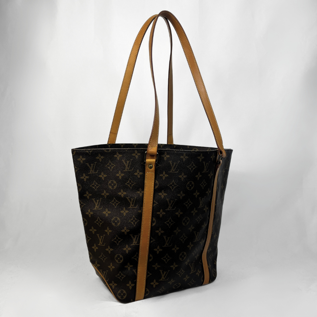 A Louis Vuitton tote bag in dark brown monogram canvas with tan leather shoulder straps and trim, photographed against a light gray studio background.