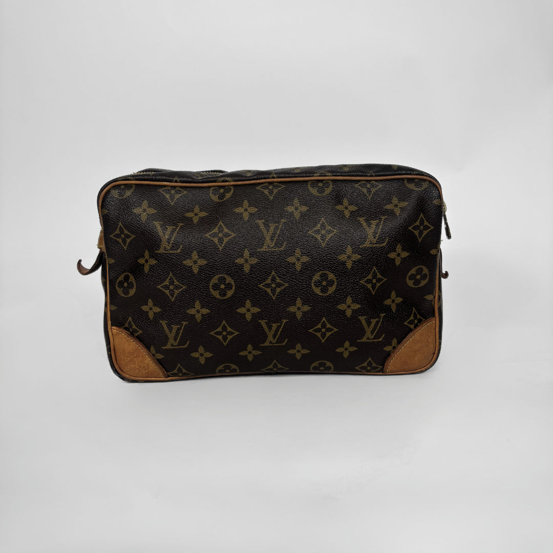 A Louis Vuitton monogram canvas toiletry bag with brown leather corner protectors, photographed against a neutral light gray background.