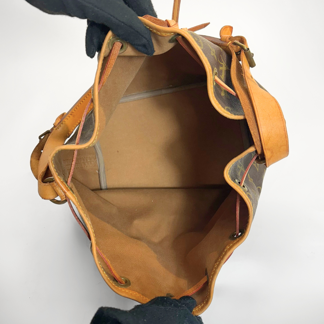 Brown leather handbag with visible brand pattern held by a gloved hand on a white background