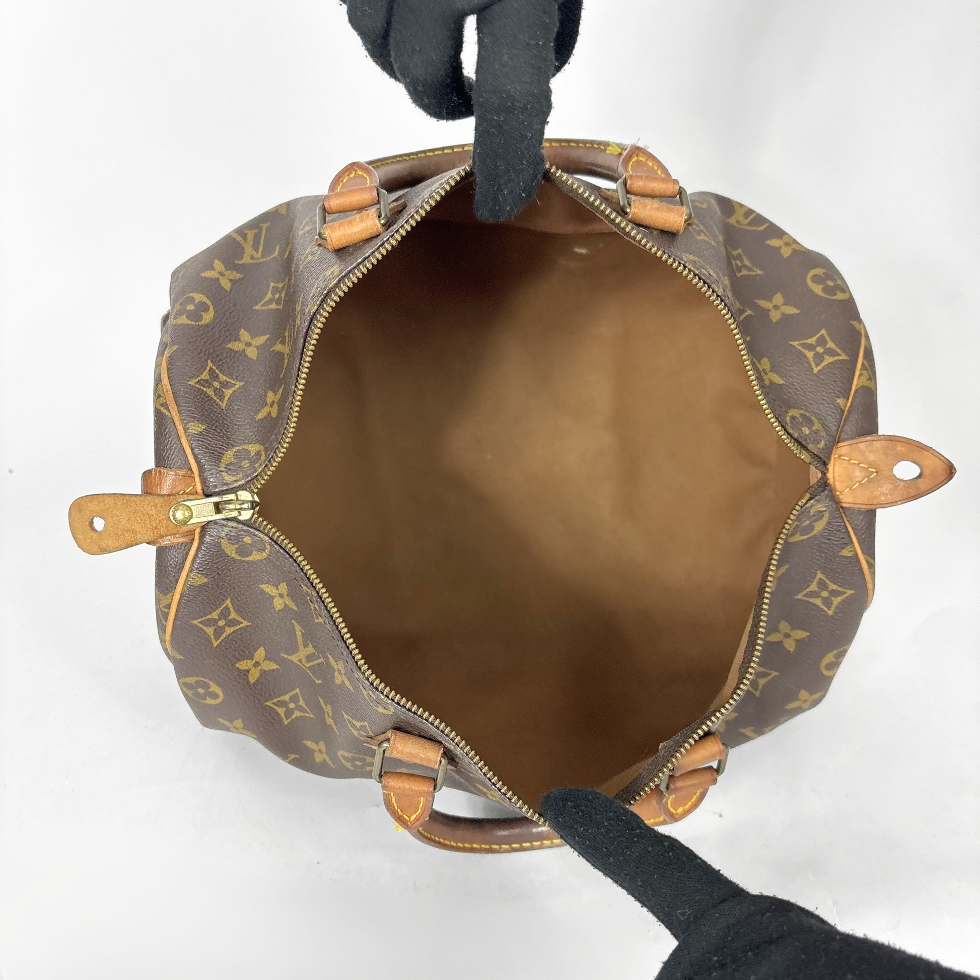 Bolso de piel marrón con estampado de monograma dorado sobre fondo blanco.