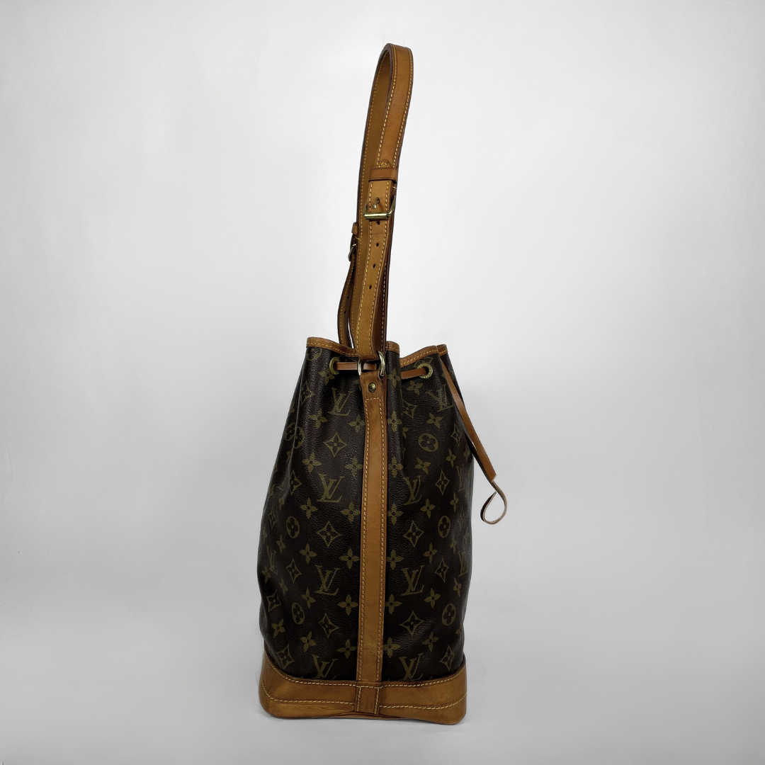 Louis Vuitton monogram canvas bucket bag with tan leather trim and shoulder strap, shown against a light gray background.