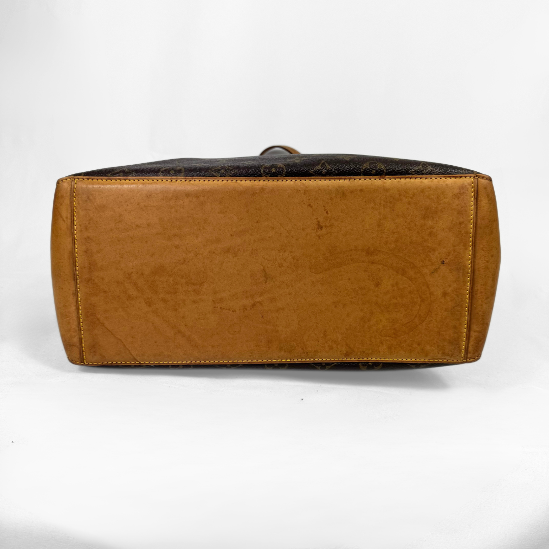 A Louis Vuitton monogram canvas and tan leather top-handle satchel shown from the back, displaying the dark brown monogram pattern and the tan leather base on a white background.