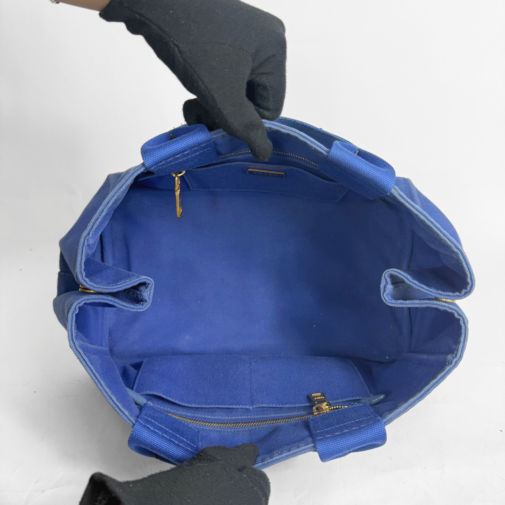 Blue bag with gold zippers held open by a gloved hand on a white background
