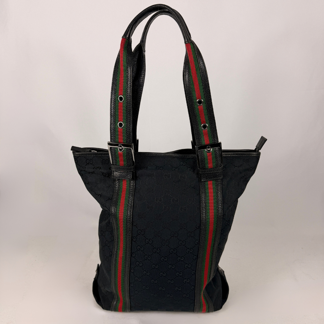 A black Gucci tote bag with the brand's signature green and red web stripe detailing on the handles and front panel, set against a plain light gray background.