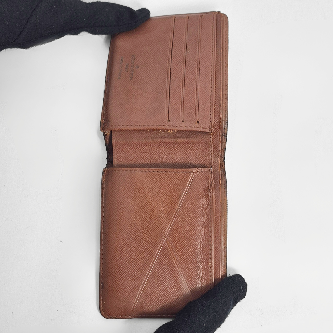 Brown leather wallet held by a gloved hand on a white background