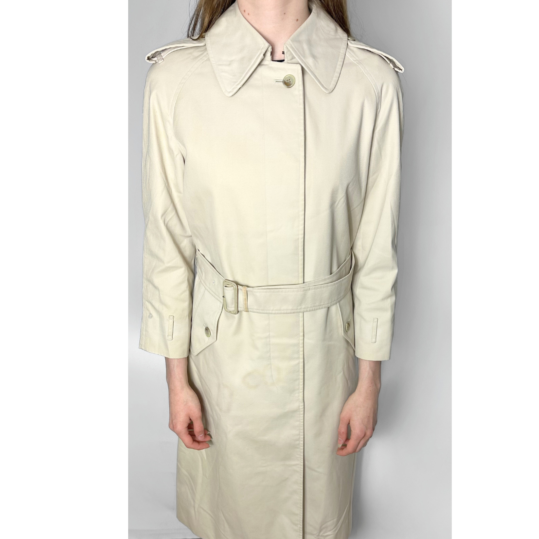 Beige trench coat worn by a person on a plain background