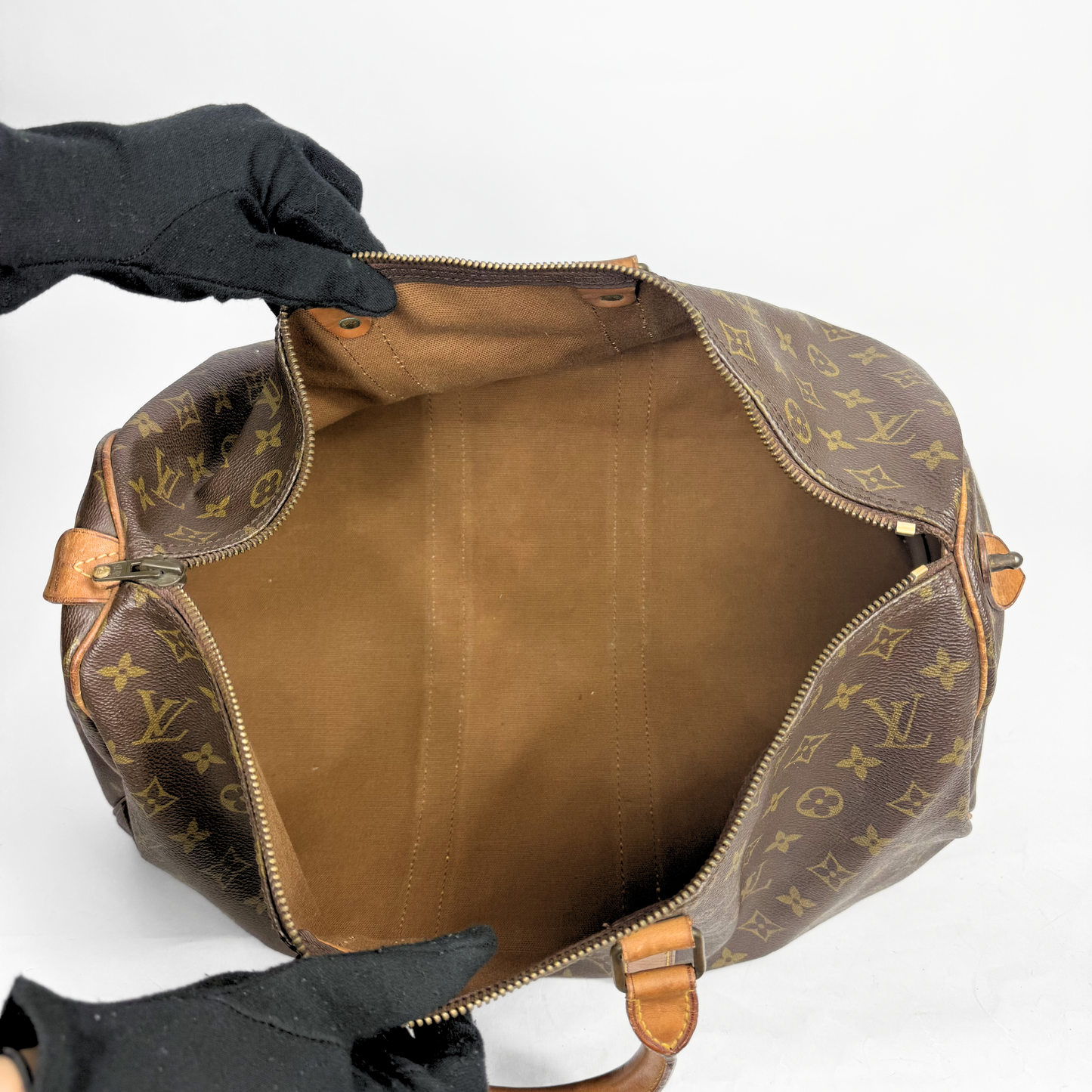 Brown Louis Vuitton bag with monogram pattern held open by a gloved hand on a white background