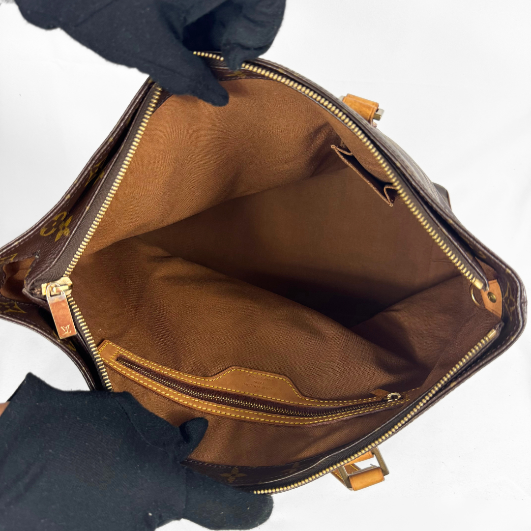An open Louis Vuitton monogram handbag shown from the inside, with a black gloved hand holding it open against a plain white background.