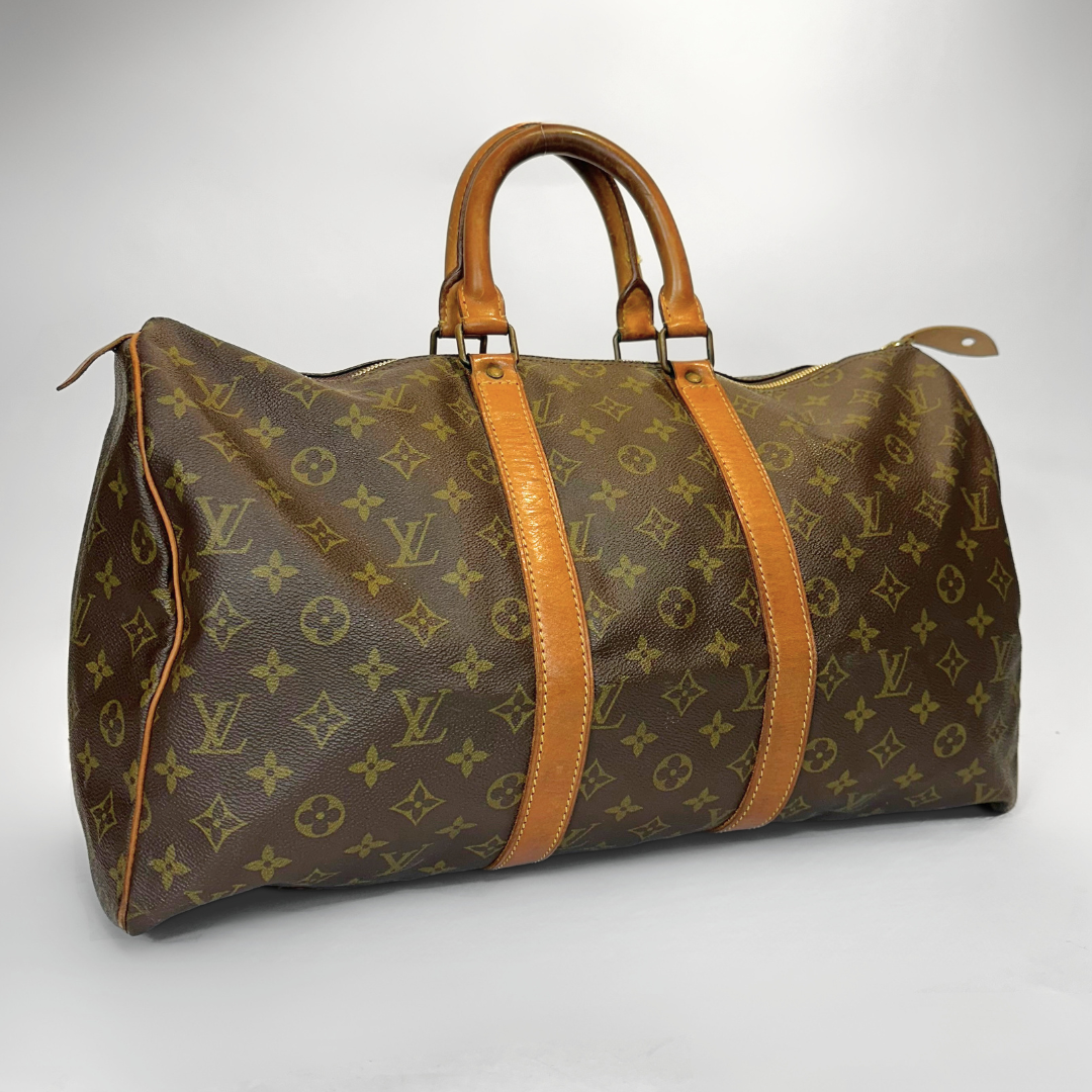 Brown monogrammed travel bag with tan leather handles and straps on a white background