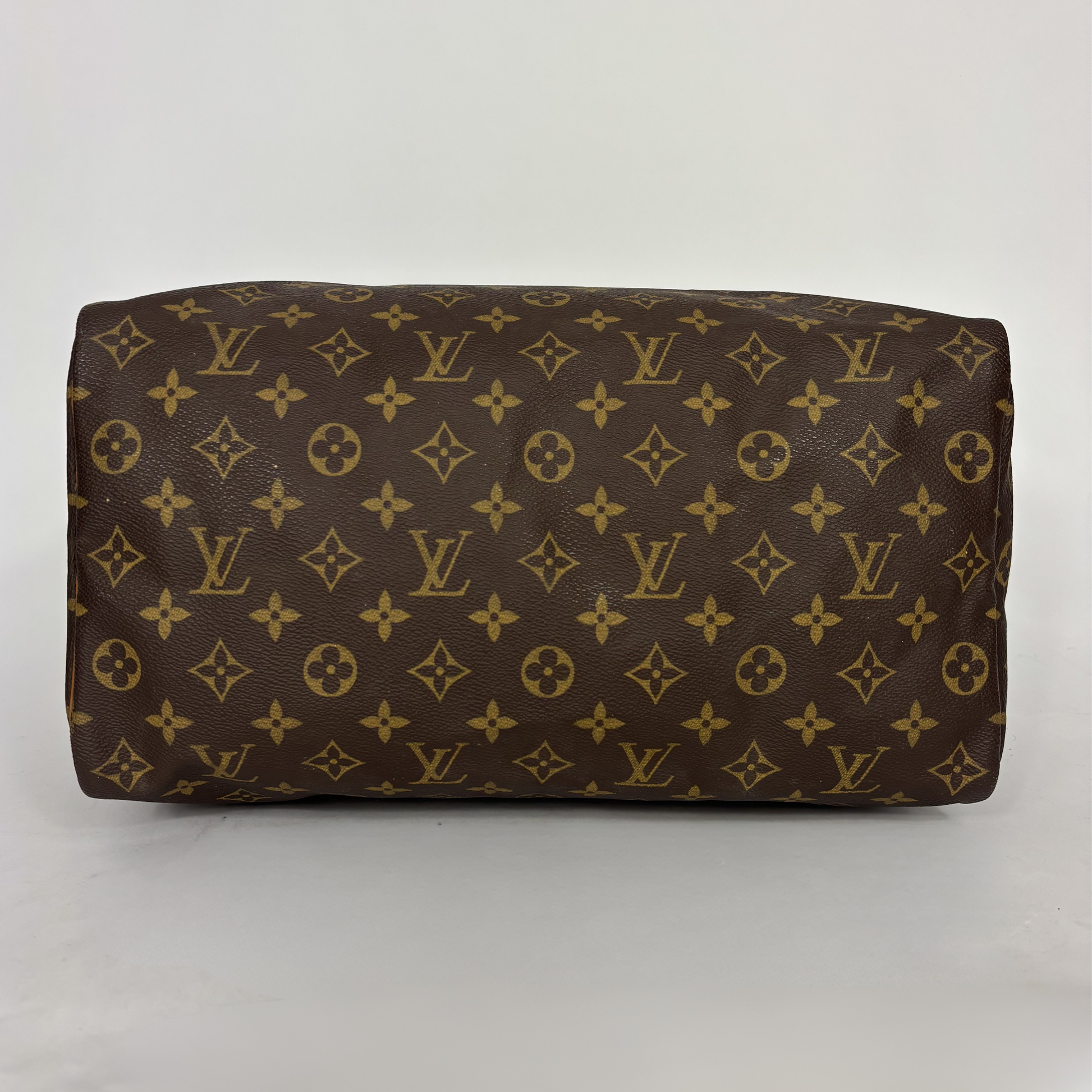 Bolso de piel marrón con estampado de monograma dorado sobre fondo blanco.