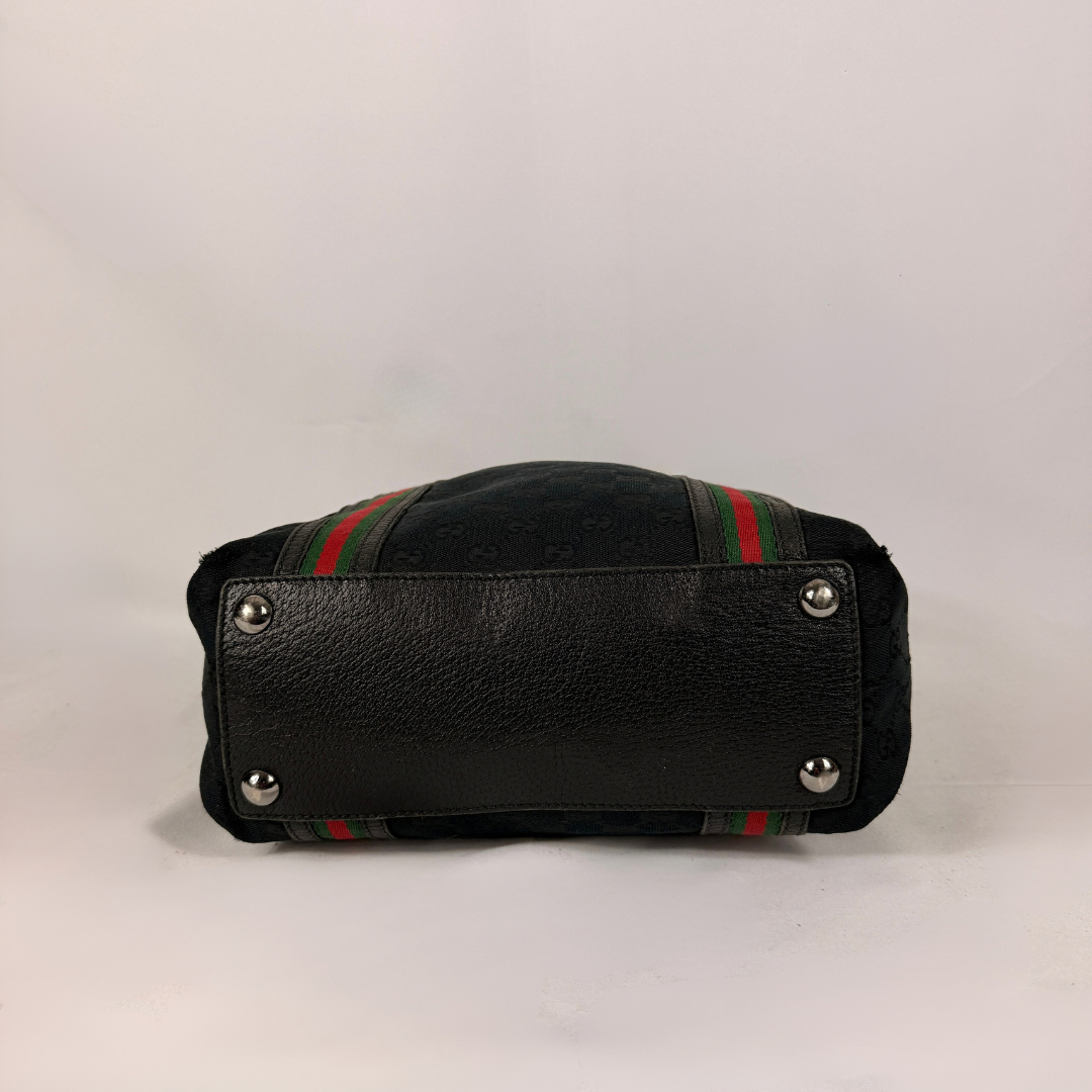 Bottom view of the Gucci Canvas Web Joy Large Tote bag featuring the signature Gucci Web stripe detailing, displayed on a light grey background.