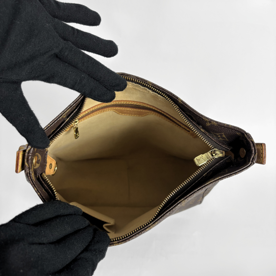 A brown monogram handbag shown open from above, with a beige interior lining and gold-tone zipper hardware. Two black gloves are holding the bag open against a plain light background.