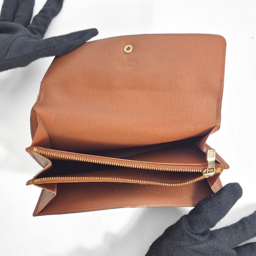 Brown leather clutch with gold zipper and clasp, held by a gloved hand on a white background