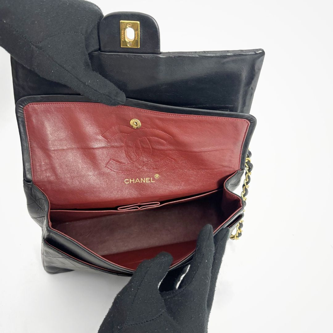 Black Chanel handbag with red interior being held open by black gloves on a white background