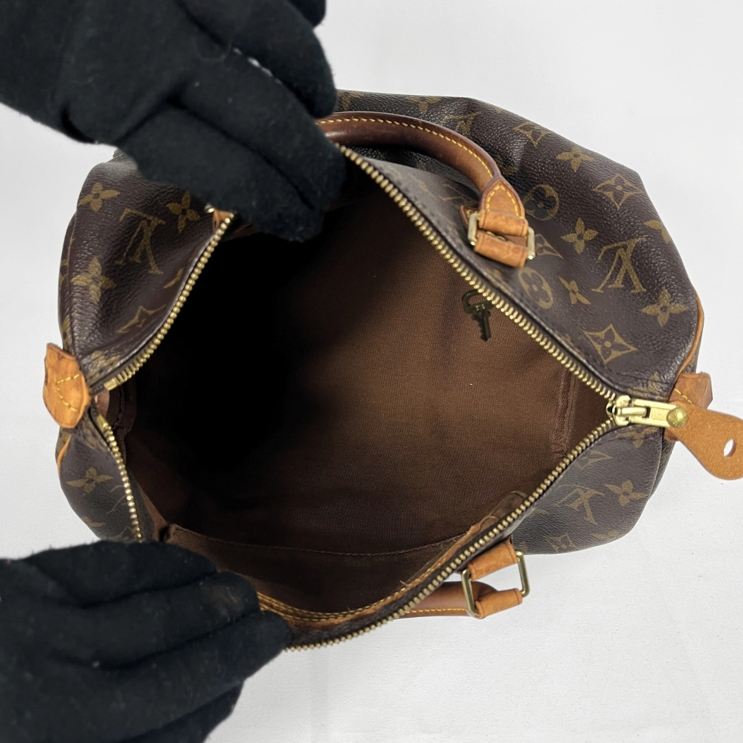 A Louis Vuitton monogram canvas Speedy handbag in dark brown with tan leather handles and trim, photographed against a light gray studio background.