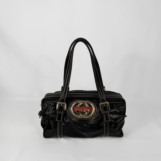 Gucci Borsa Dialux Britt Boston nell'iconica tela Dialux, esposta su uno sfondo grigio chiaro.