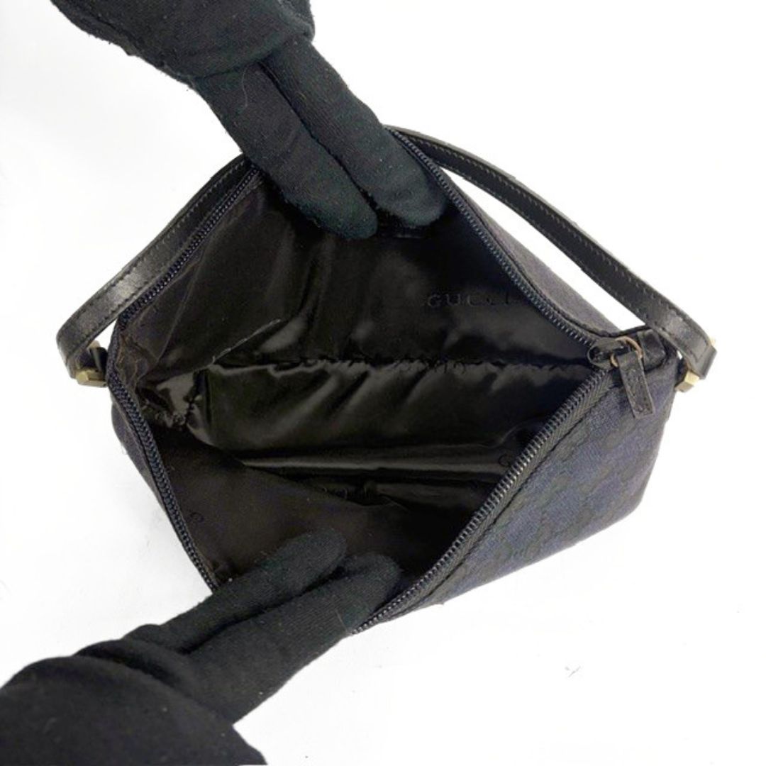 Black handbag with open lid held by gloved hands on a white background