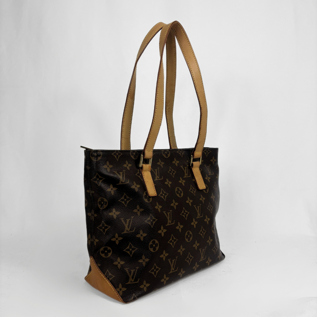 A Louis Vuitton monogram canvas tote bag with tan leather shoulder straps and trim, shown from a three-quarter angle against a light gray studio background.