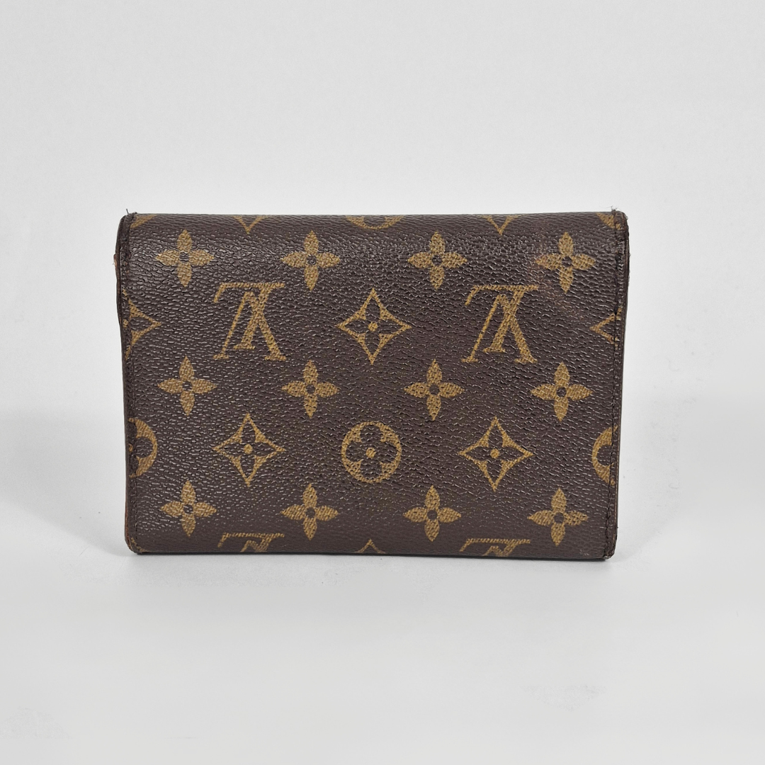 Cartera marrón con estampado de monograma dorado sobre fondo blanco.