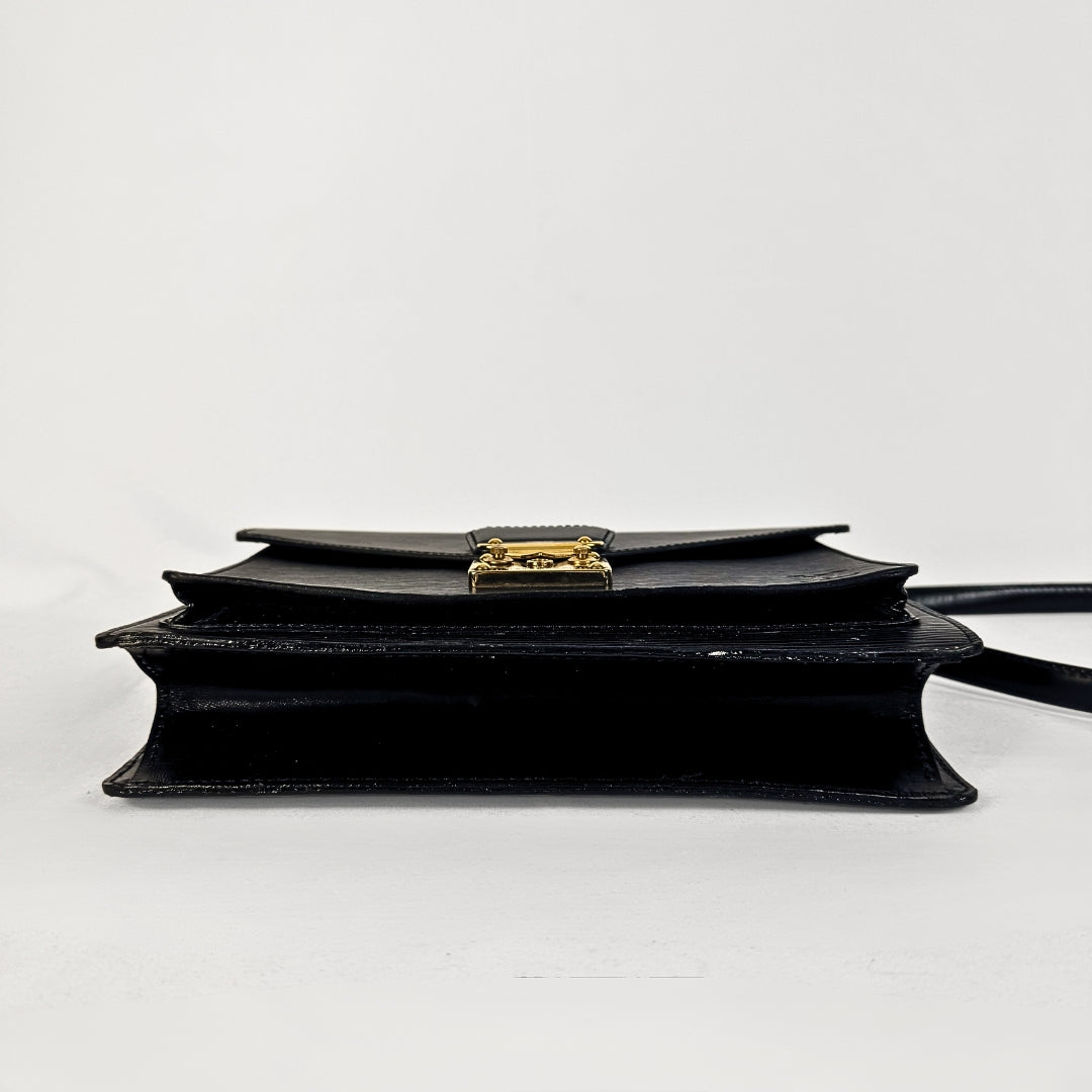 A black leather book-style clutch bag with a gold-tone metal clasp, shown from a side profile view against a plain white background.