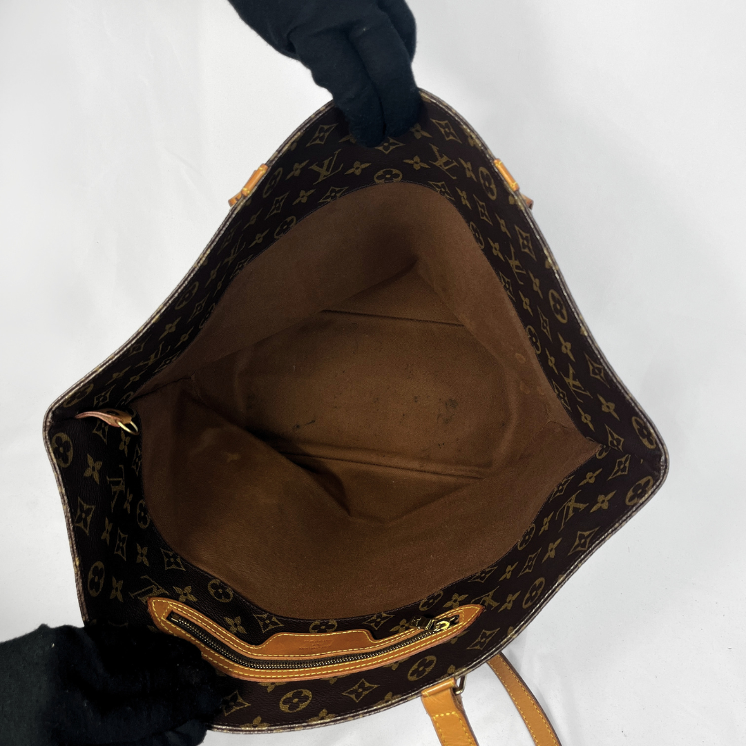 A Louis Vuitton monogram canvas tote bag shown open from the top, with a black gloved hand holding it against a plain white background.
