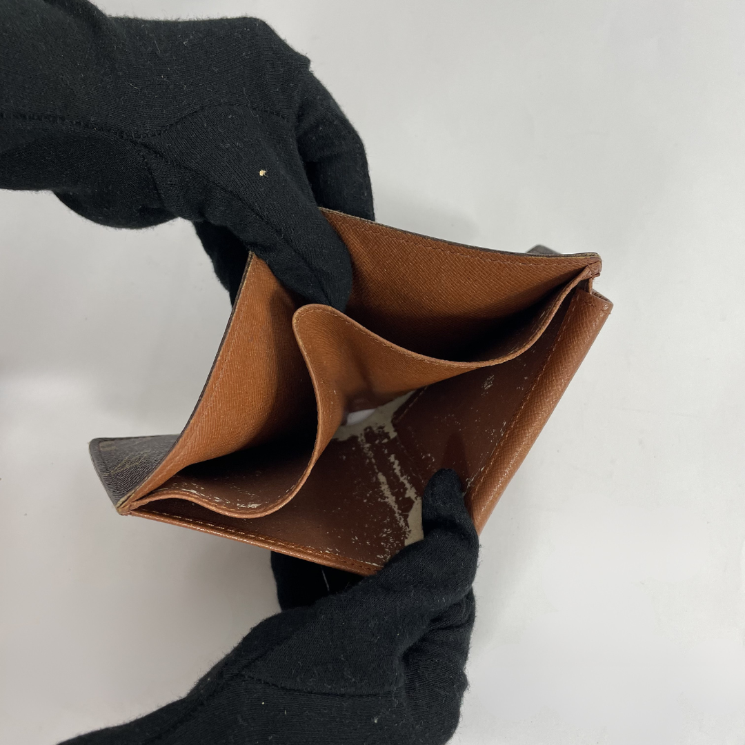A brown leather wallet held open by two hands wearing black knit gloves, shown against a plain light gray background.
