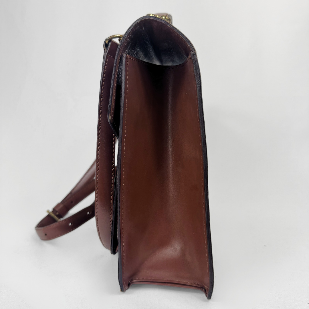 A brown leather shoulder bag shown from a side profile view, featuring a dark brown interior lining and a matching brown strap with gold-tone hardware, set against a plain white background.
