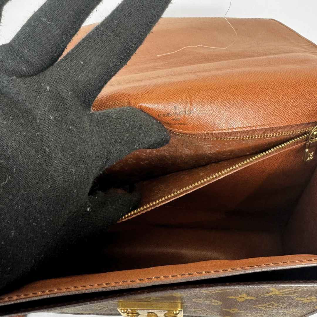 Close-up of a Louis Vuitton monogram handbag interior with a black glove lifting the flap to show the tan Vachetta leather lining and gold-tone zipper.
