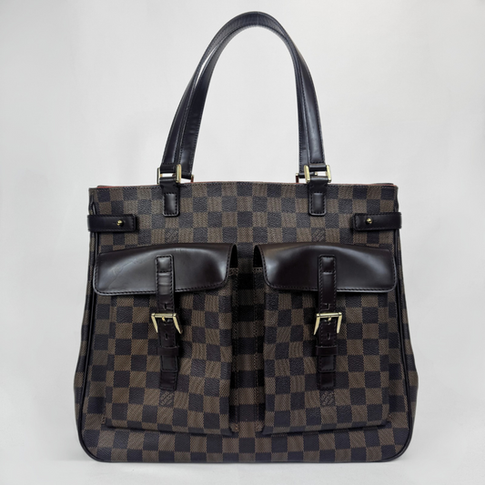 A Louis Vuitton Tragetasche aus Damier Ebene Canvas mit dunkelbraunen Ledergriffen und -besatz, zwei praktischen Vordertaschen mit Schnallendetails, vor einem schlichten hellgrauen Hintergrund.