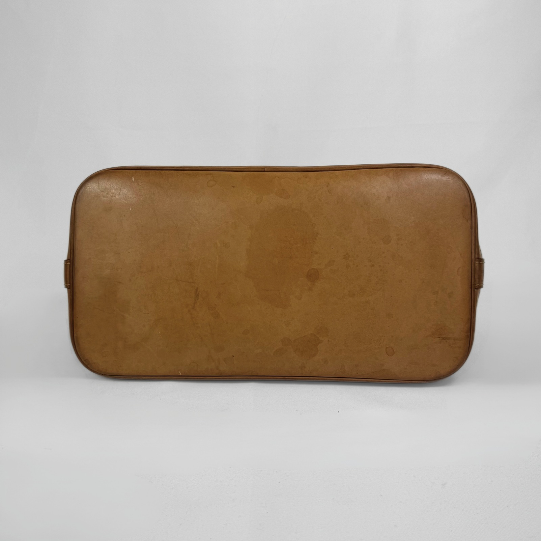 A vintage tan leather suitcase or travel case shown from the back, featuring a rounded rectangular shape and a weathered, stained surface, set against a plain light gray background.