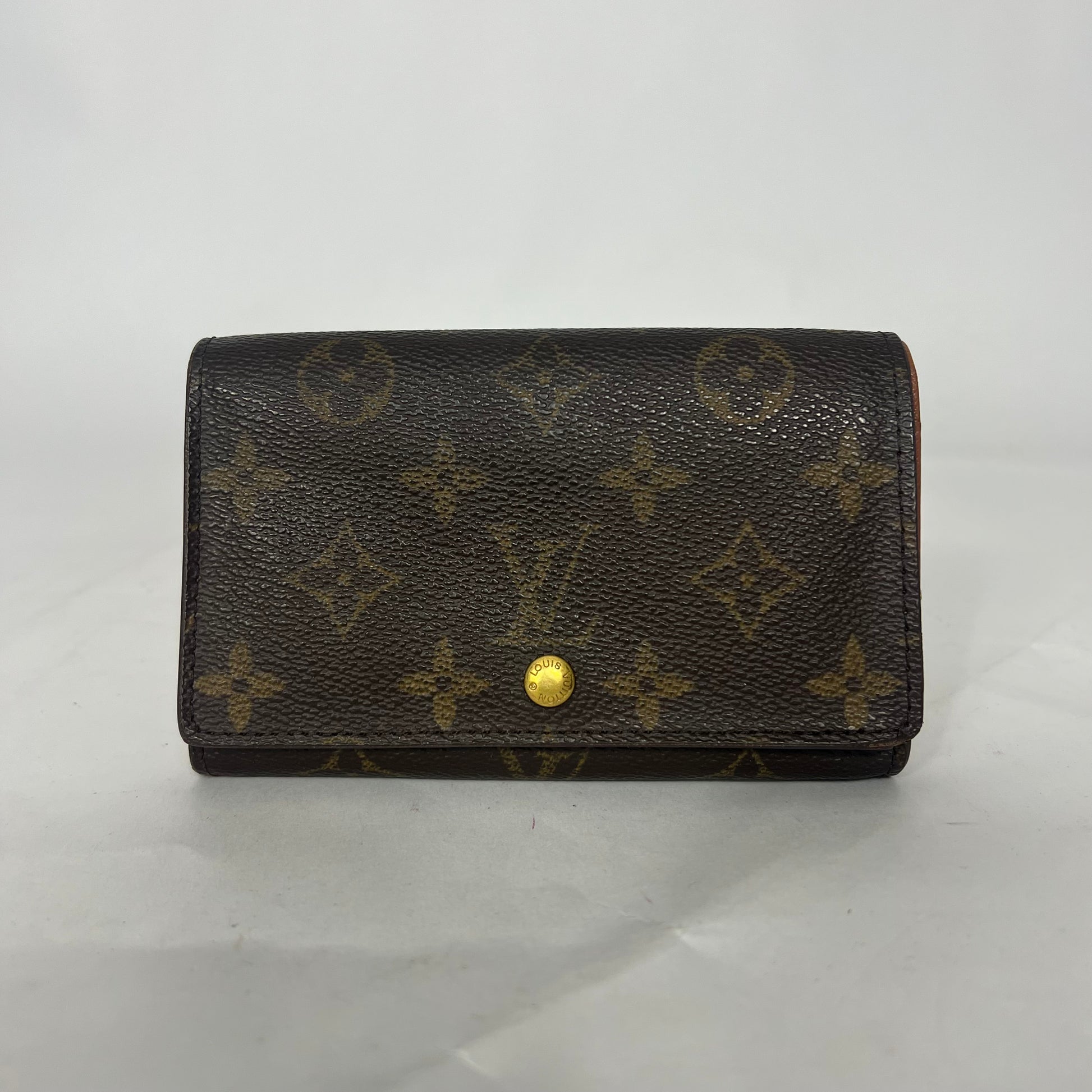 Ruskea lompakko, jossa on kultainen monogrammikuvio valkoisella taustalla