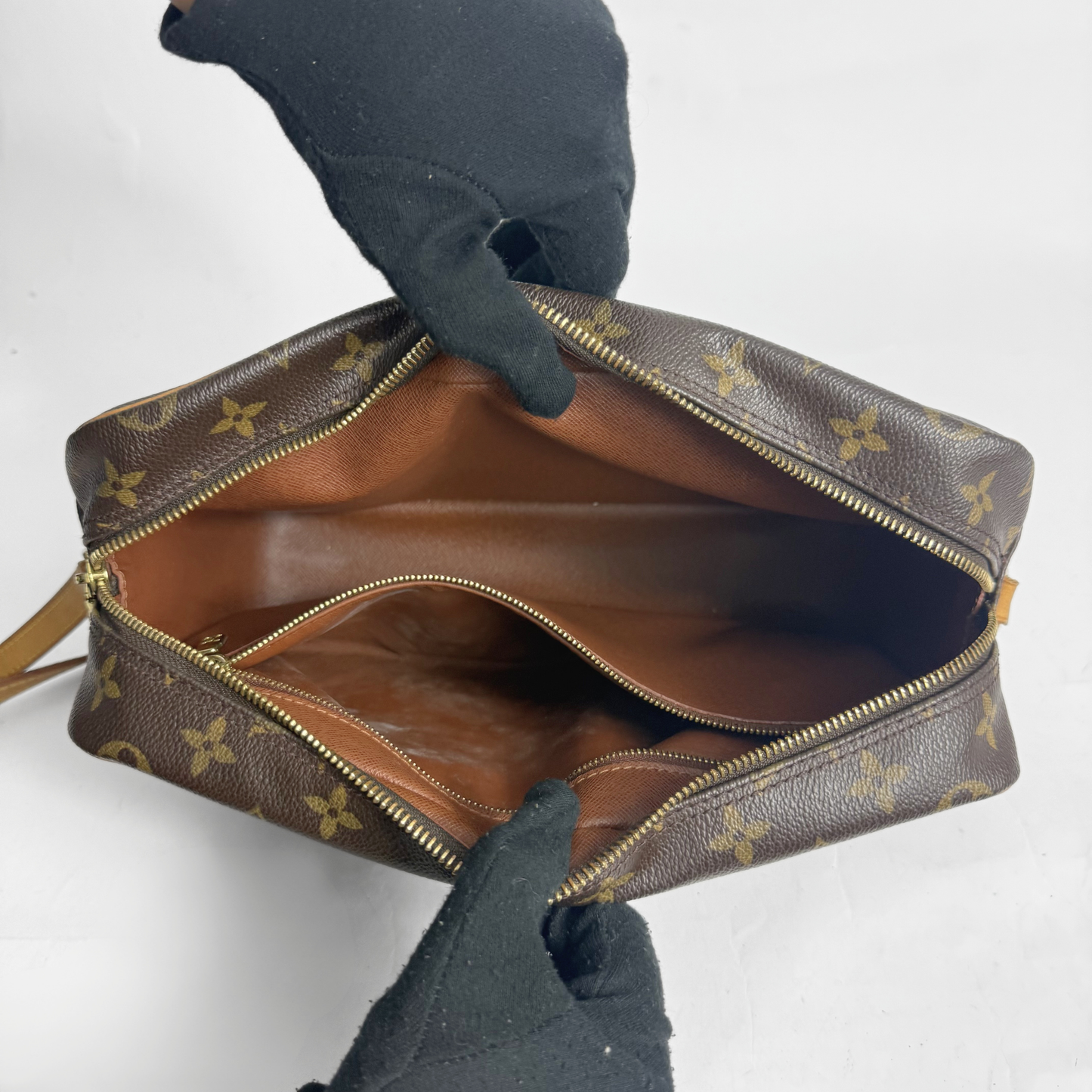 Brown handbag with gold monogram pattern held by gloved hands on a white background